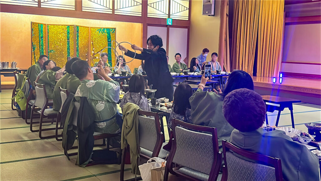 富士山温泉ホテル鐘山苑の宴会場にてリングマジックを披露するCrystal Magician® Michelとリングを持って参加するインドネシア人のゲスト