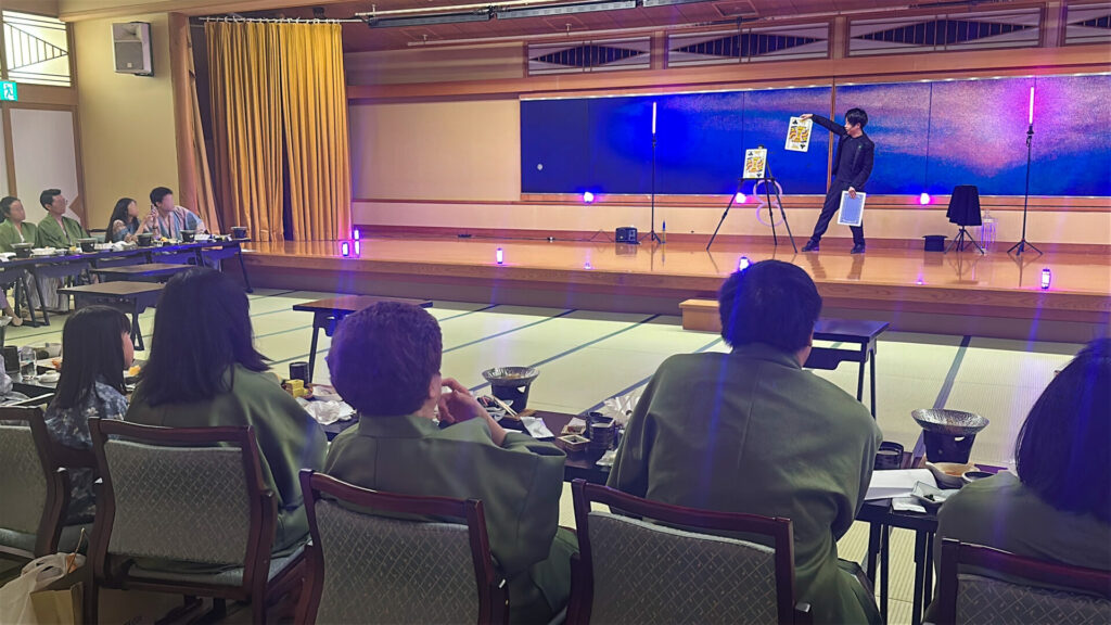 富士山温泉ホテル鐘山苑の宴会場ステージにて大きな３枚のトランプを使ったマジックを演じるCrystal Magician® Michelとそれを観るゲスト