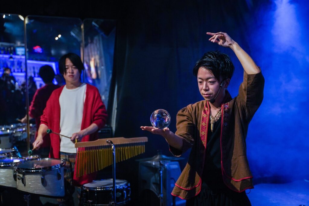 2026/1/7神奈川県茅ヶ崎市Studio ONEにて青い照明の下で水晶玉を使ったコンタクトジャグリングを披露するCrystal Magician® Michel