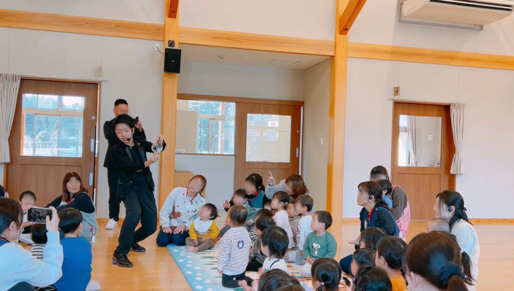 栃木県那須塩原市のひがしなす保育園で客席の間を歩きながら水晶玉パフォーマンスを披露するCrystal Magician® Michelとそれを観る子どもたち