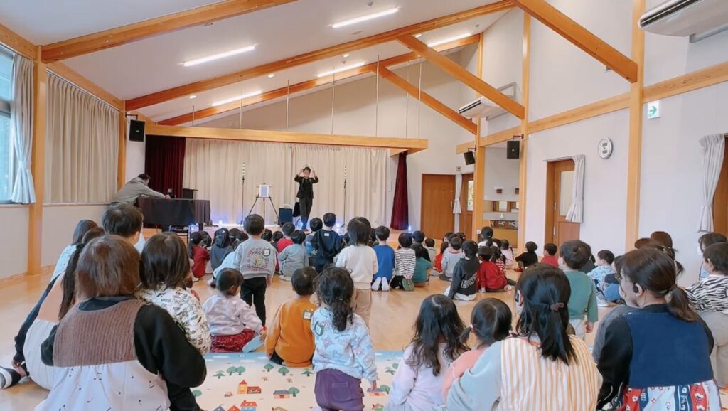 栃木県那須塩原市のひがしなす保育園でLED演出とともに金属のリングを使ったステージマジックを披露するCrystal Magician® Michelとそれを観る子どもたち