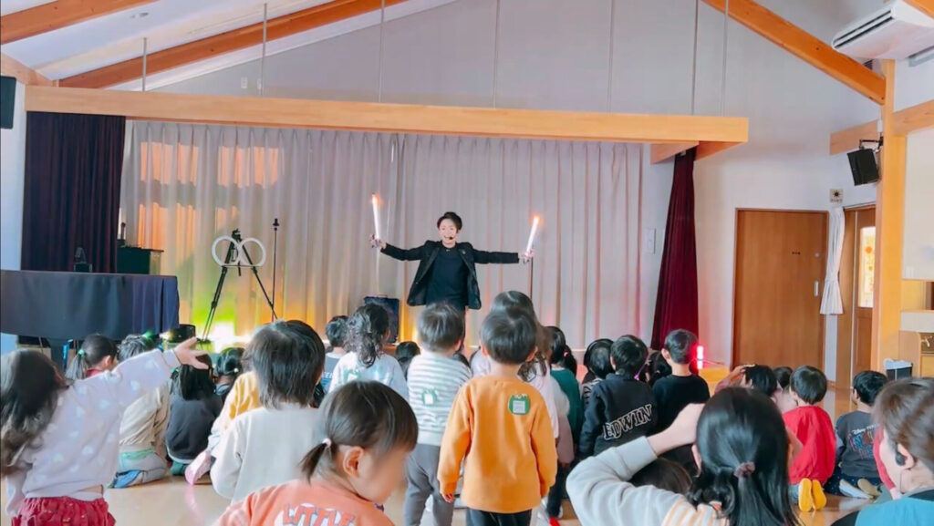 栃木県那須塩原市のひがしなす保育園でLEDパフォーマンスを披露するCrystal Magician® Michelとそれを観る子どもたち