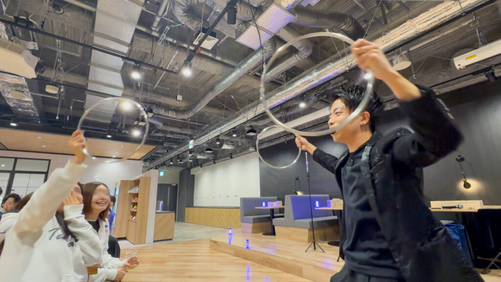 株式会社テラスカイ・テクノロジーズのオフィスで開かれた5周年記念イベントにて、LED演出と共に金属のリングを使ったステージマジックを演じるCrystal Magician® Michelと、リングを掴んで驚くゲストの様子