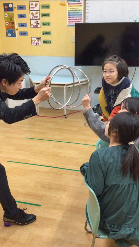 2026/1/5KidsDuo戸塚駅前のウィンタースクールイベントにて金属のリングを使ったステージマジックを披露するCrystal Magician® Michelとリングを掴んで参加する子ども