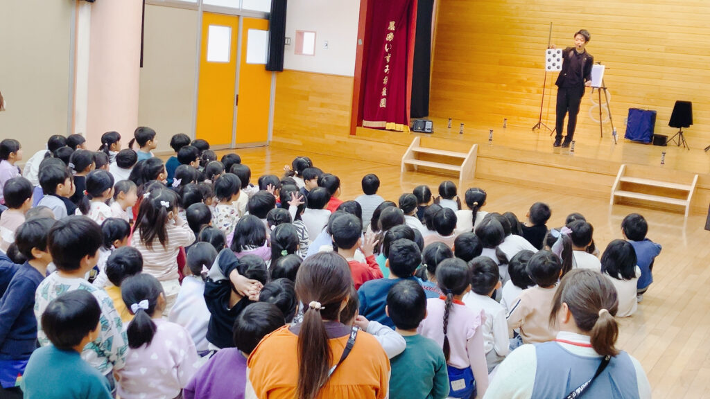 栃木県那須塩原市の黒磯いずみ幼稚園で黒い点が移動するマジックを演じるCrystal Magician® Michelと参加する子どもたち