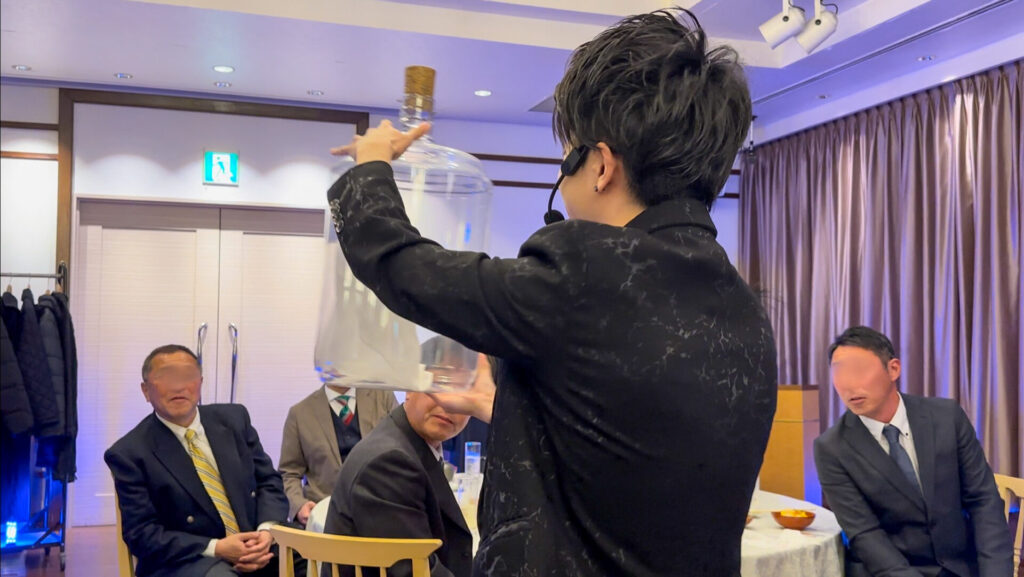 2026年2月2日、ザ・ウィングス海老名で開かれた海老名トラック地区会新年会にてボトルの中をハンカチが自在に動くマジックを披露するCrystal Magician® Michelが会場をボトルと共に歩き回る様子